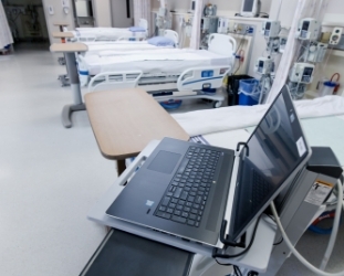 A computer sitting on a table. There are a row of hospital beds in the background