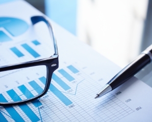 A page with bar charts on it. A pen and a pair of black glasses is on top