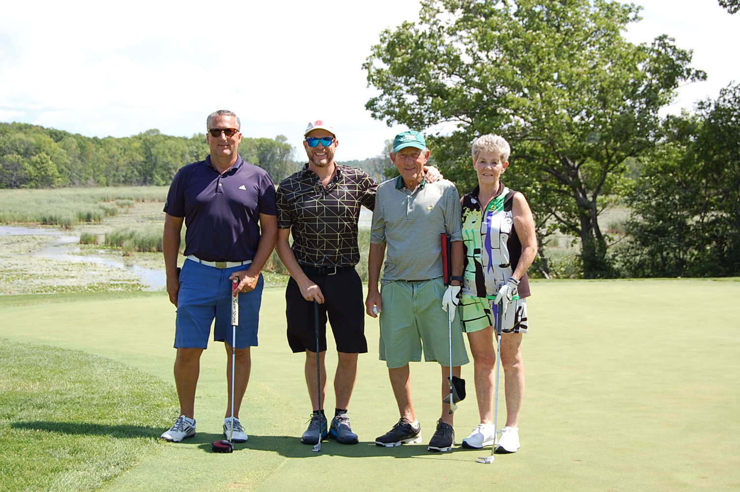 Three men and a woman on a golf green in their golf clothes