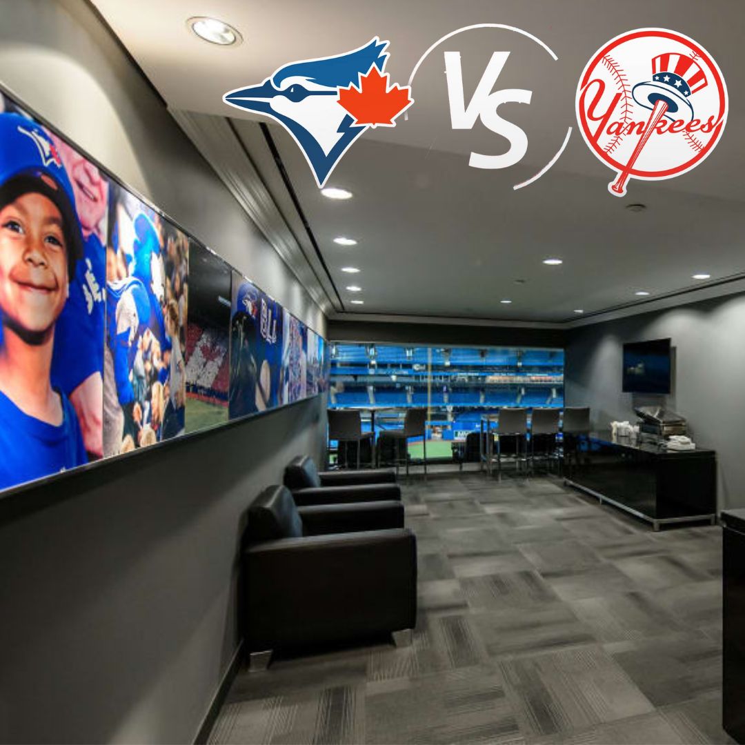 A room with black comfortable arm chairs, a TV set and chairs and table looking out a window at a baseball field. Images of The Toronto Blue Jays fans are on the wall and the Blue Jays logo and the New York Yankees logo are at the top.
