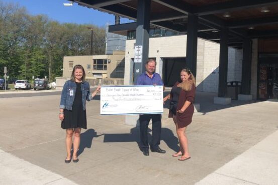Two woman and a man hold up a giant cheque for $20,000 standing outside the emergency entrance to GBGH.