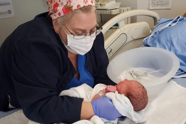 a nurse in a colourful head scarf lifting a new born baby off a bed