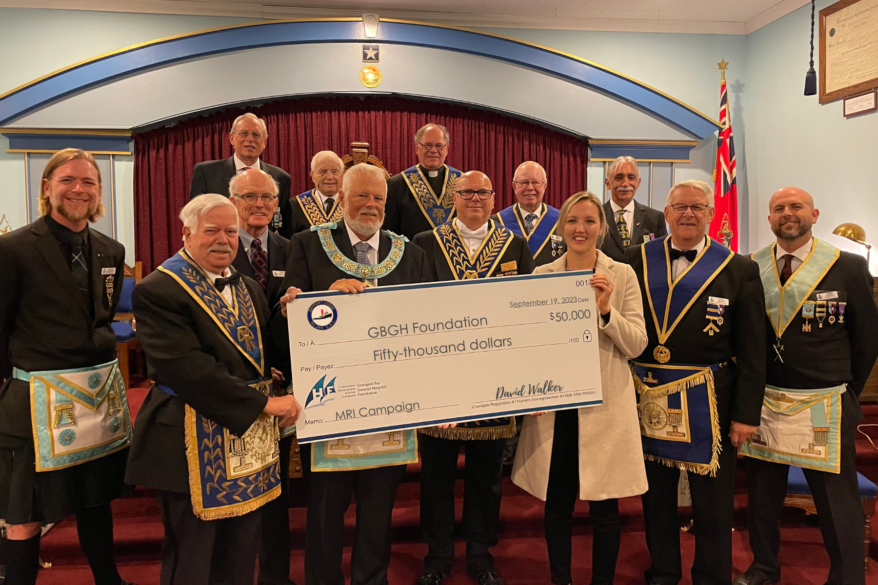 Twelve men wearing Lodge regalia present a giant cheque to a women who represents the GBGH Foundation for $50, 000 from the Bayfort Lodge