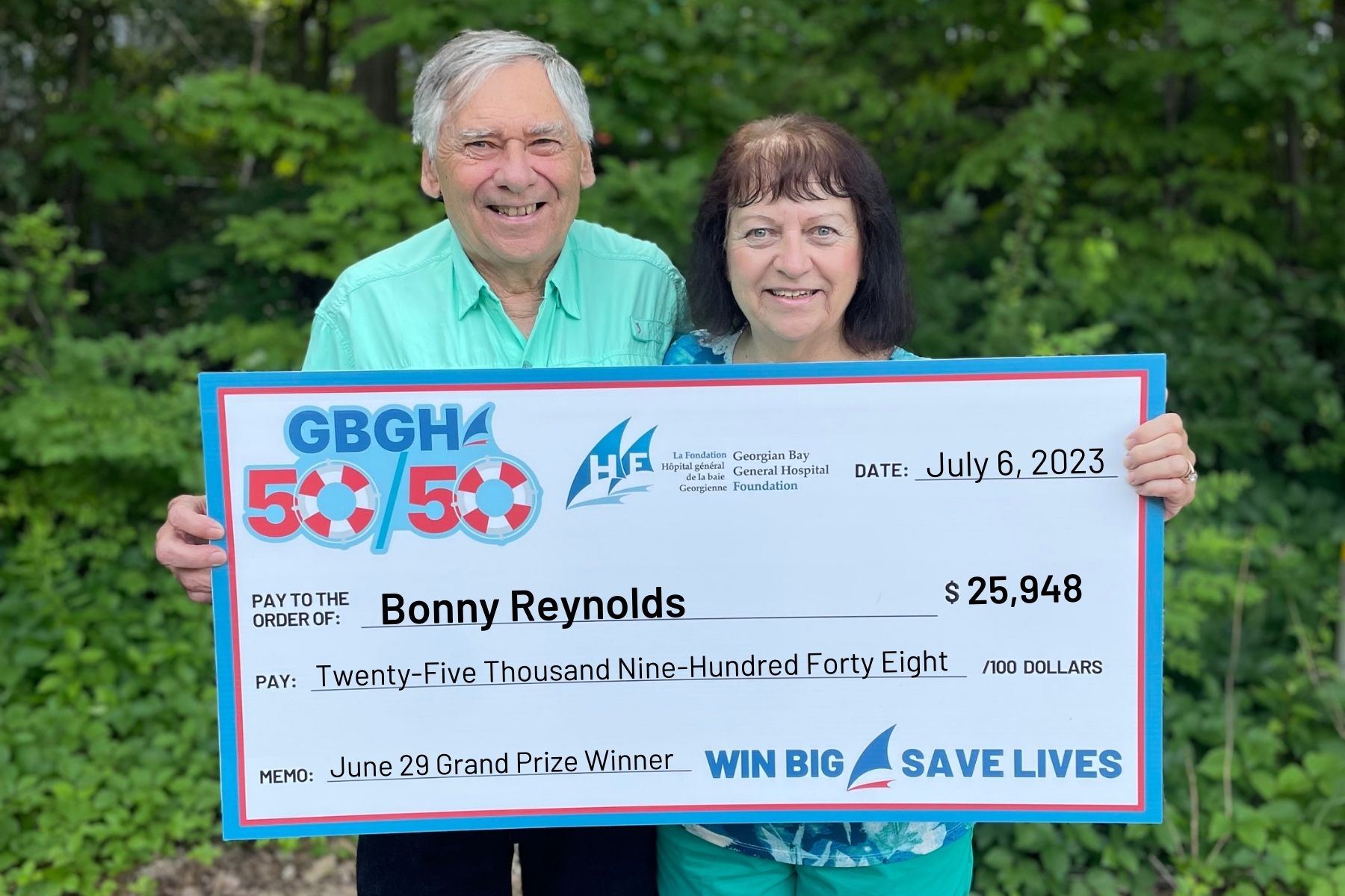 Bonney Reynolds and a man hold up a cheque for $25,948 presented for winning the June 50/50 draw.