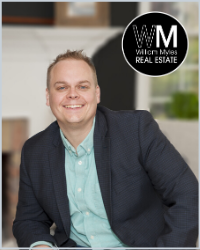 A blonde Man in a green shirt and dark jacket . the WM Real Estate logo is above