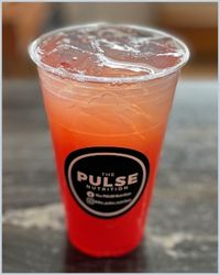 A plastic glass with bright orange liquide. A round black logo that says Pulse Nutrition is on the glass.