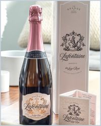 A bottle of champagne with a pink foil top and two white branded bags