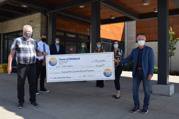 Seven people in masks standing 2 feet apart. 2 are holding a giant cheque for $10,000 from the Town of Midland to the GBGH Foundation