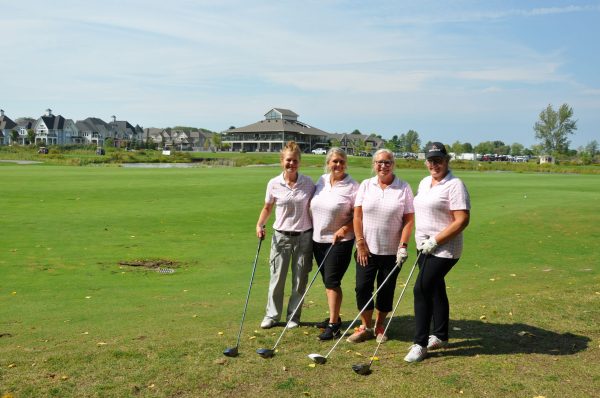Four women on the golf course all wearing pink golf shirts.