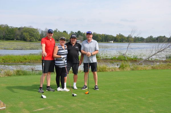 Three men and a women on a golf course green. A large body of swamp area is behind them.
