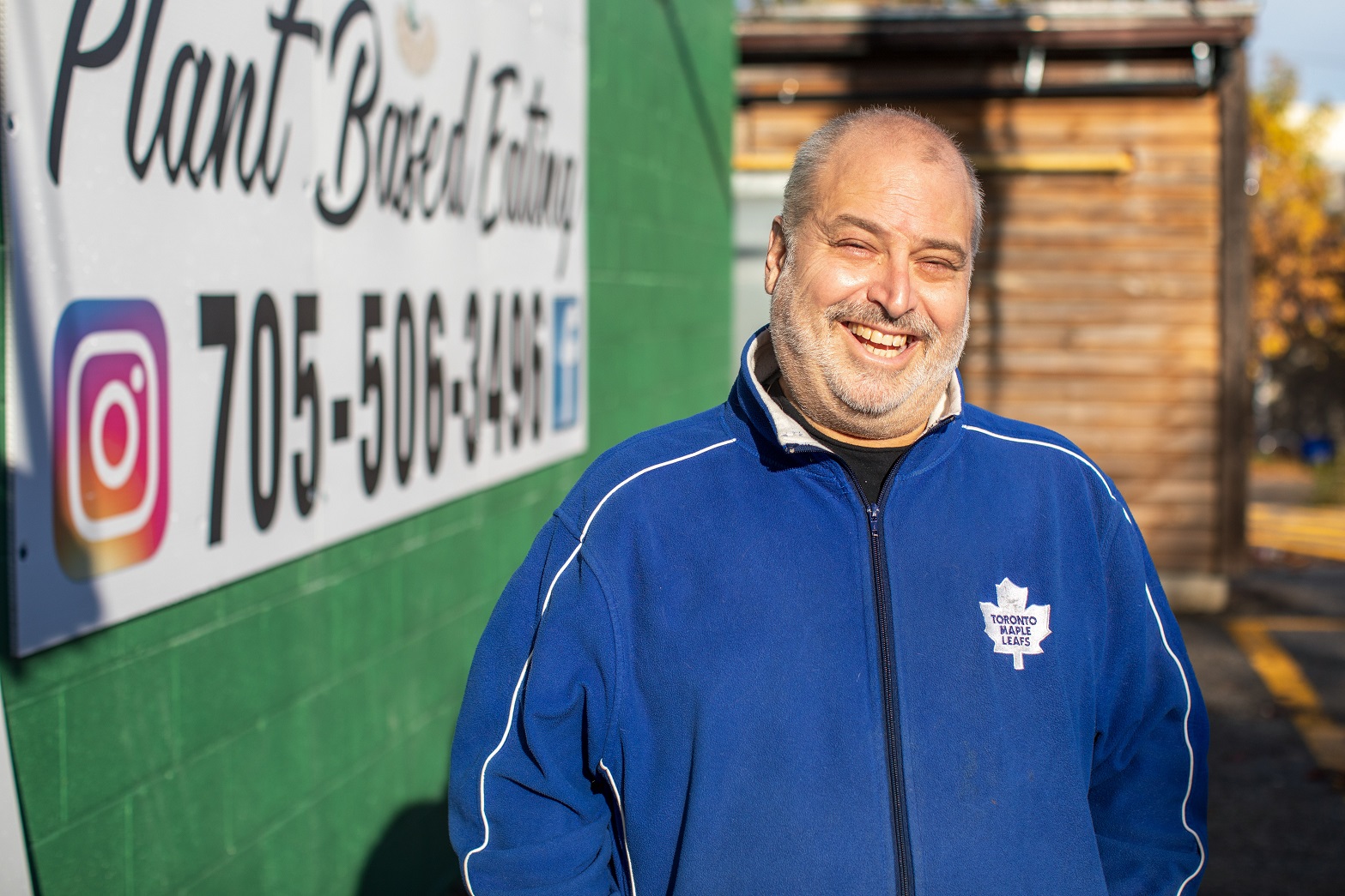 A smiling grey haired man with a receding hair line and short trimmed beard wearing a blue Toronto Maple Leafs jacket.