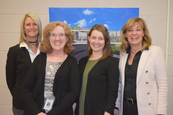 Four smiling women posing in front of a picture of the front of GBGH