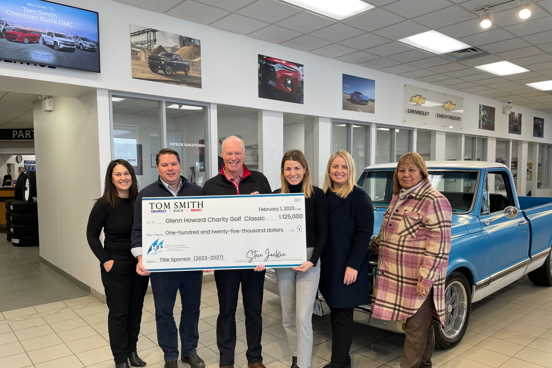 Two women and four men hold a giant cheque made out to the Glenn Howard Charity Classic for $125,000 from Tom Smith Motors