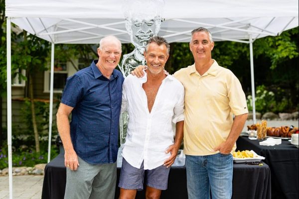 Three men pose in front of an outside food tent.