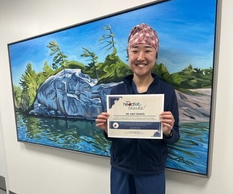 A woman is blue scrubs and a brown print head scarf holds up a Heartfelt Thanks certificate