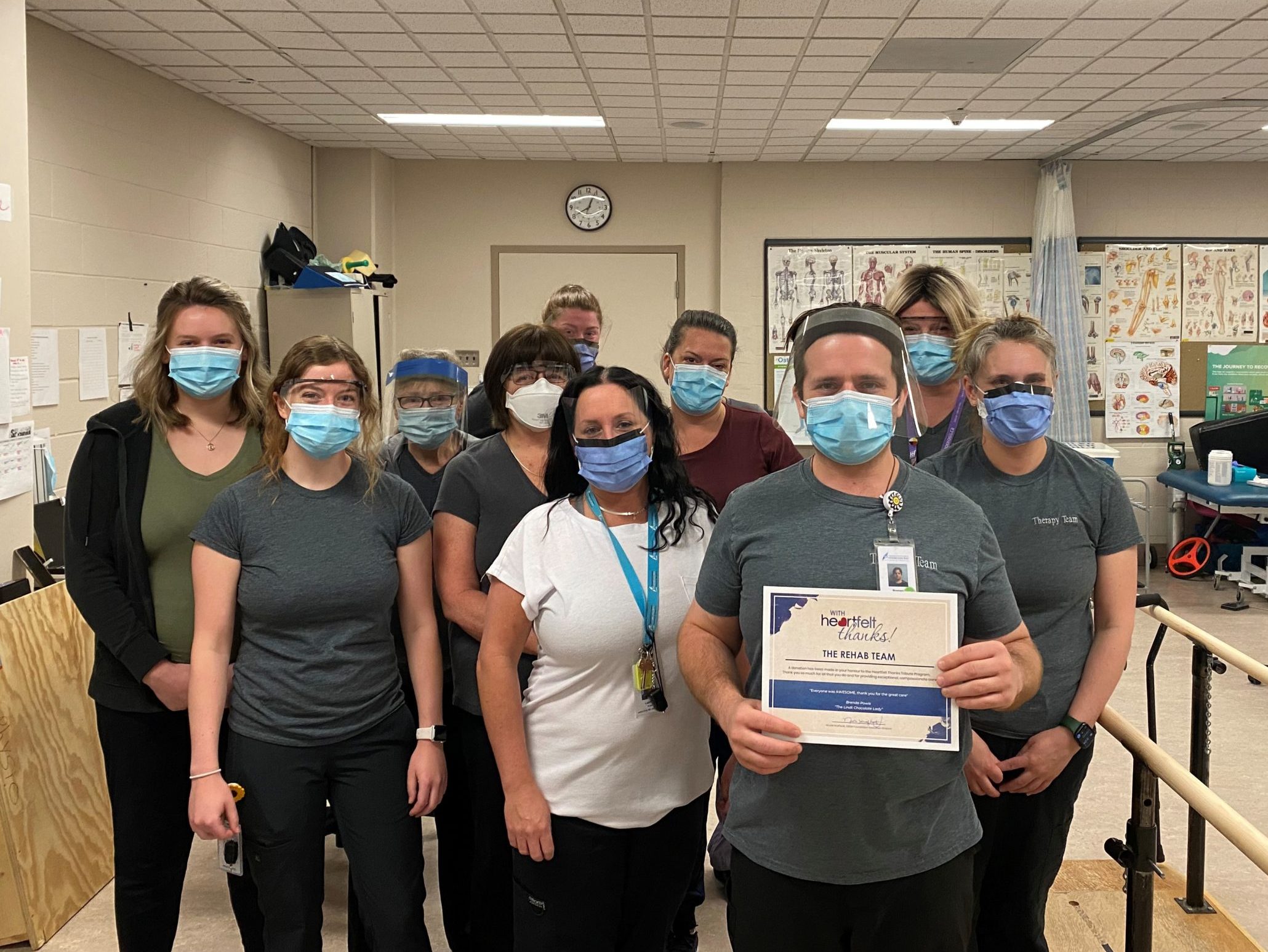 Ten men and woman wearing masks hold up a Heartfelt Thanks certificate for the Rehab Team