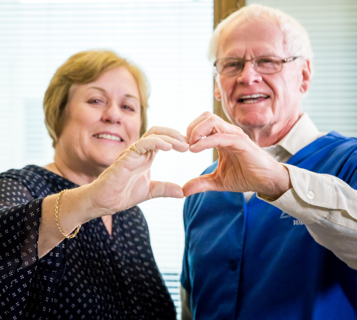 An older man and woman putting their fingers together to make a heart shape.