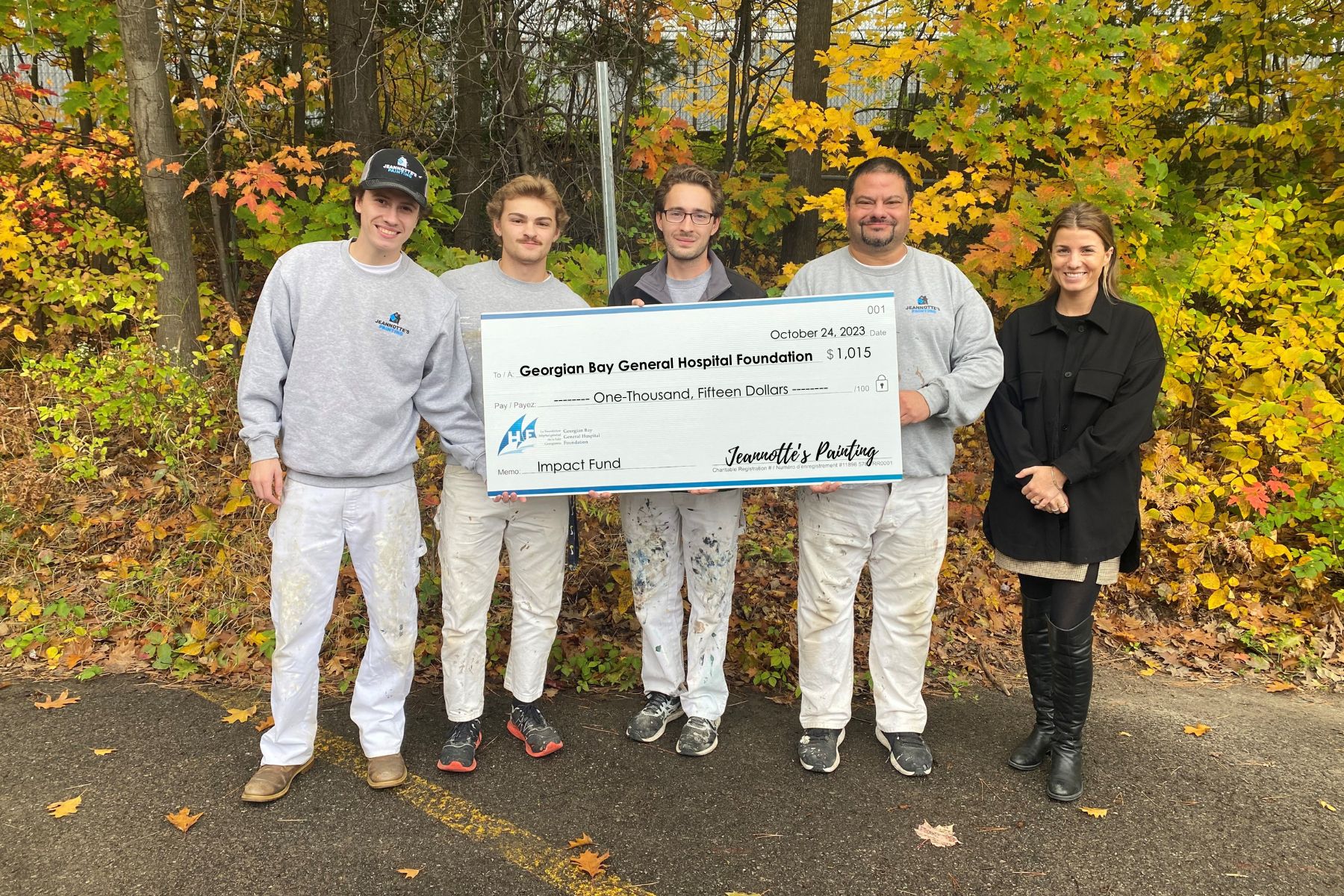Four men in grey and white paint stained clothing hold a giant cheque made out to GBGH Foundation for $1, 015 from Jeannotte's Painting. A women wearing black stands beside them.