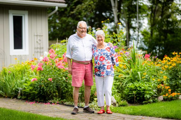 A man in n white shirt and orange shorts and a woman in a flowered top and white pants in their garden
