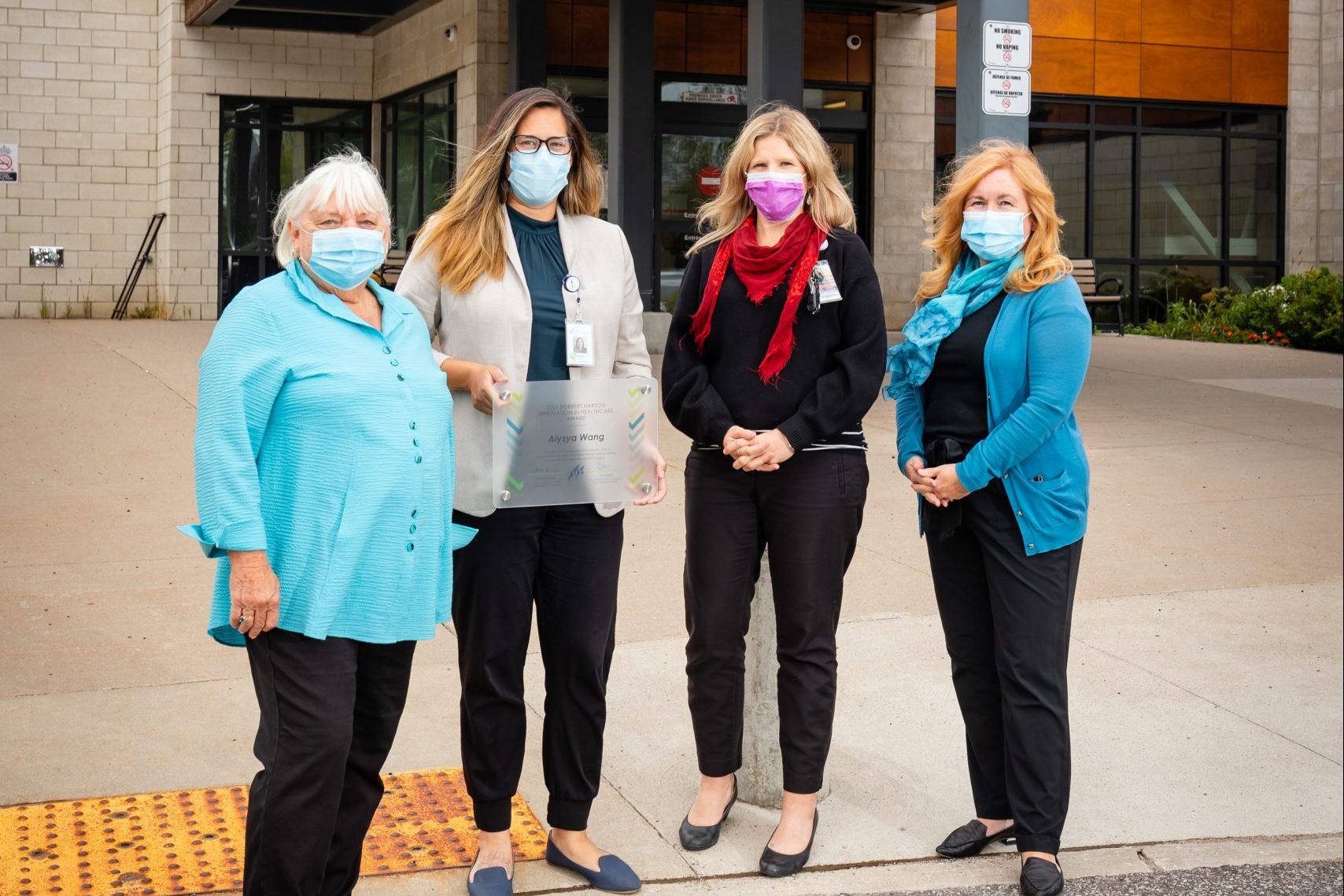 Four women in masks stand outside the hospital. One of them in holding an award plaque