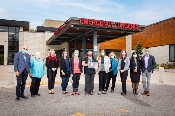 Nine women and two men in masks stand outside the hospital. Two of the women are holding award plaques