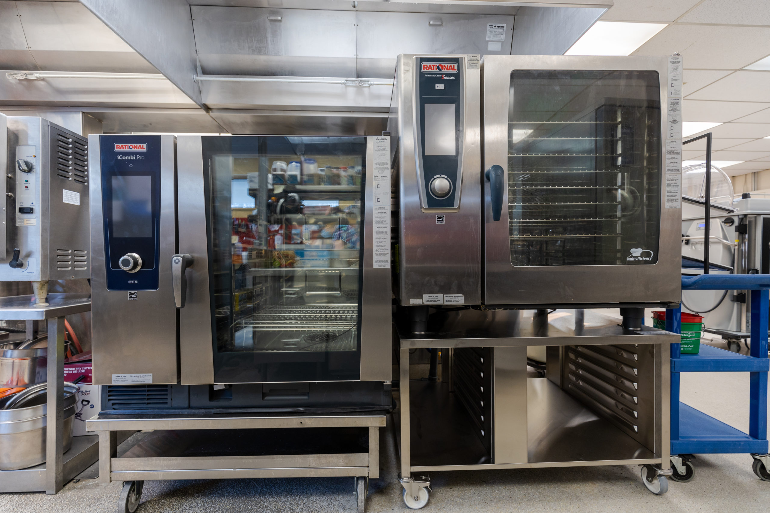 Two large metal industrial sized ovens sitting on steel rolling carts with shelves.