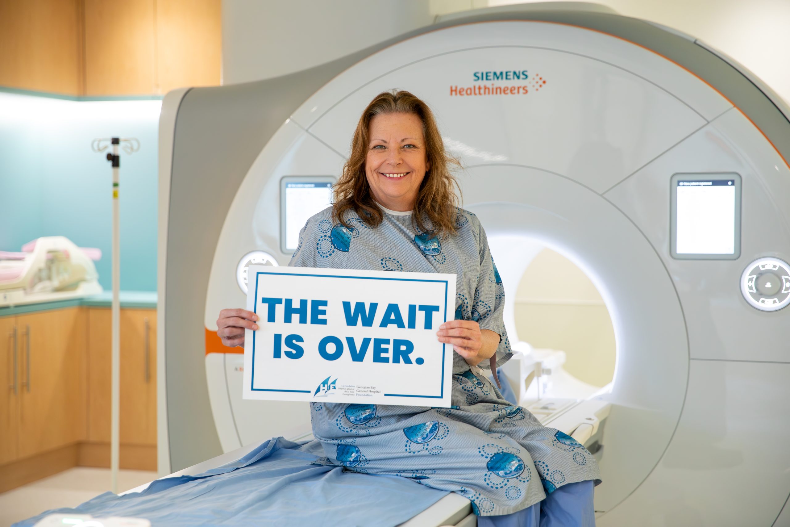 Maureen holds a sign that says "The Wait is Over" for new GBGH MRI machine.