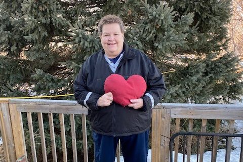 A woman with short brown hair holds a big stuffed red heart