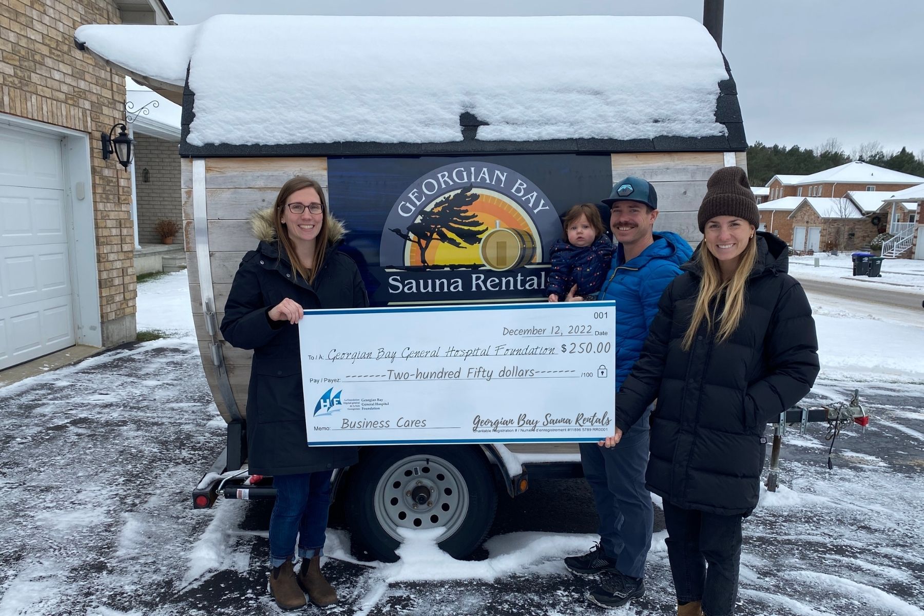 Two women, a man and a small child stand out in the snow with a giant cheque to the GBGH Foundation for $250 from Georgian Bay Sauna Rentals.