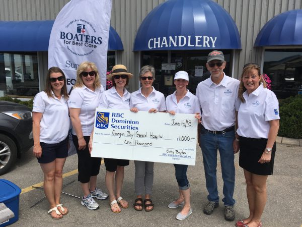 Seven people with White golf shirts hold a giant cheque for $1,000 to GBGH from Dominion Securities at Hindson Marina