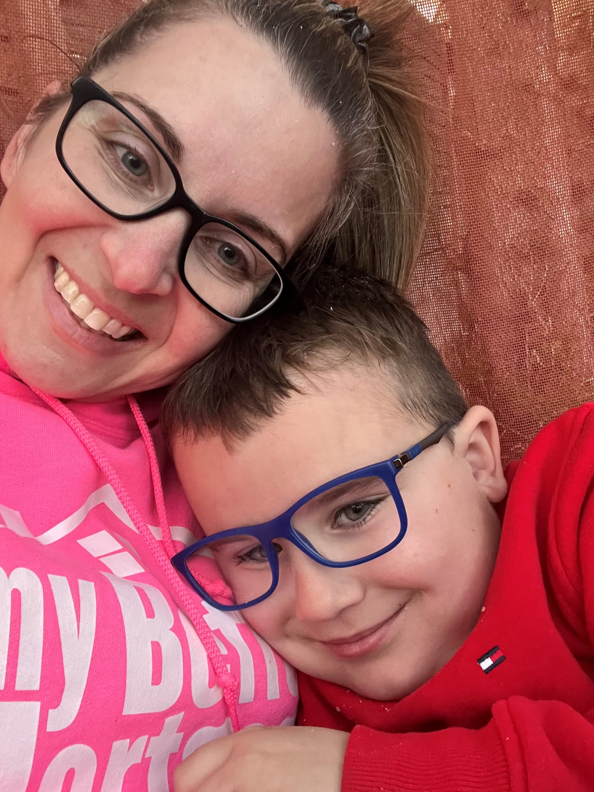 Woman wearing glasses cuddles with a boy also wearing glasses.