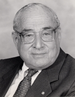 A Black and white image of an older man in a suit and tie with receding hair and wearing glasses.