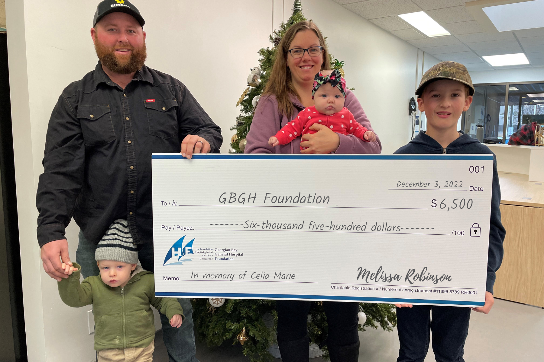 A man, a women, a young boy, a toddle and a baby stand with a giant cheque for $6,500 to the GBGH Foundation in memory of Celia Marie