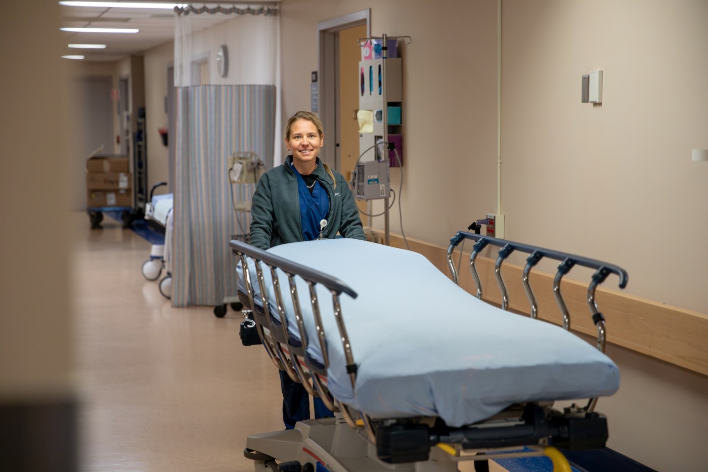 A nurse stands behind a stretcher bed in a hospital hallway