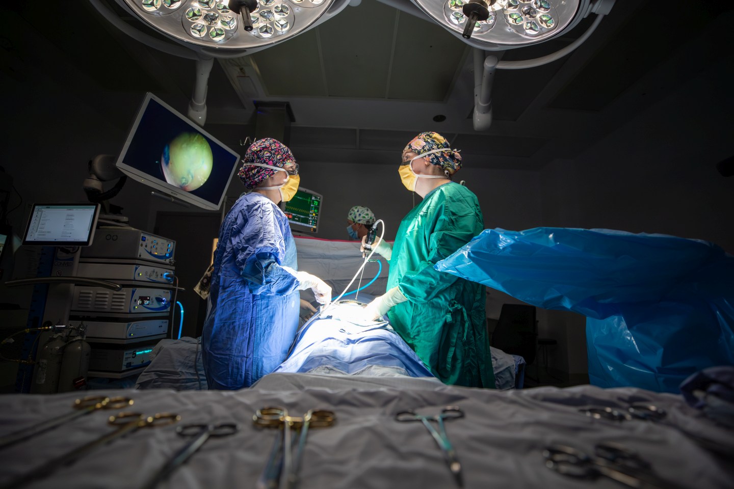 2 surgeons operating on a patient with lights overhead
