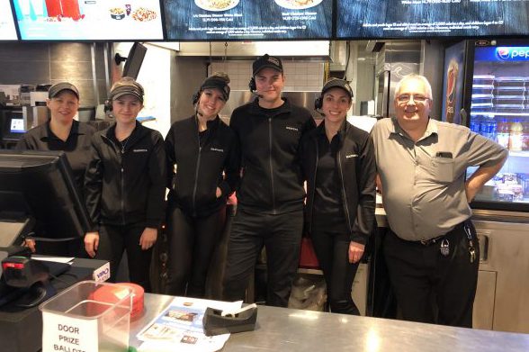 Seven Harveys restaurant employees pose in their black uniforms under the menu boards.