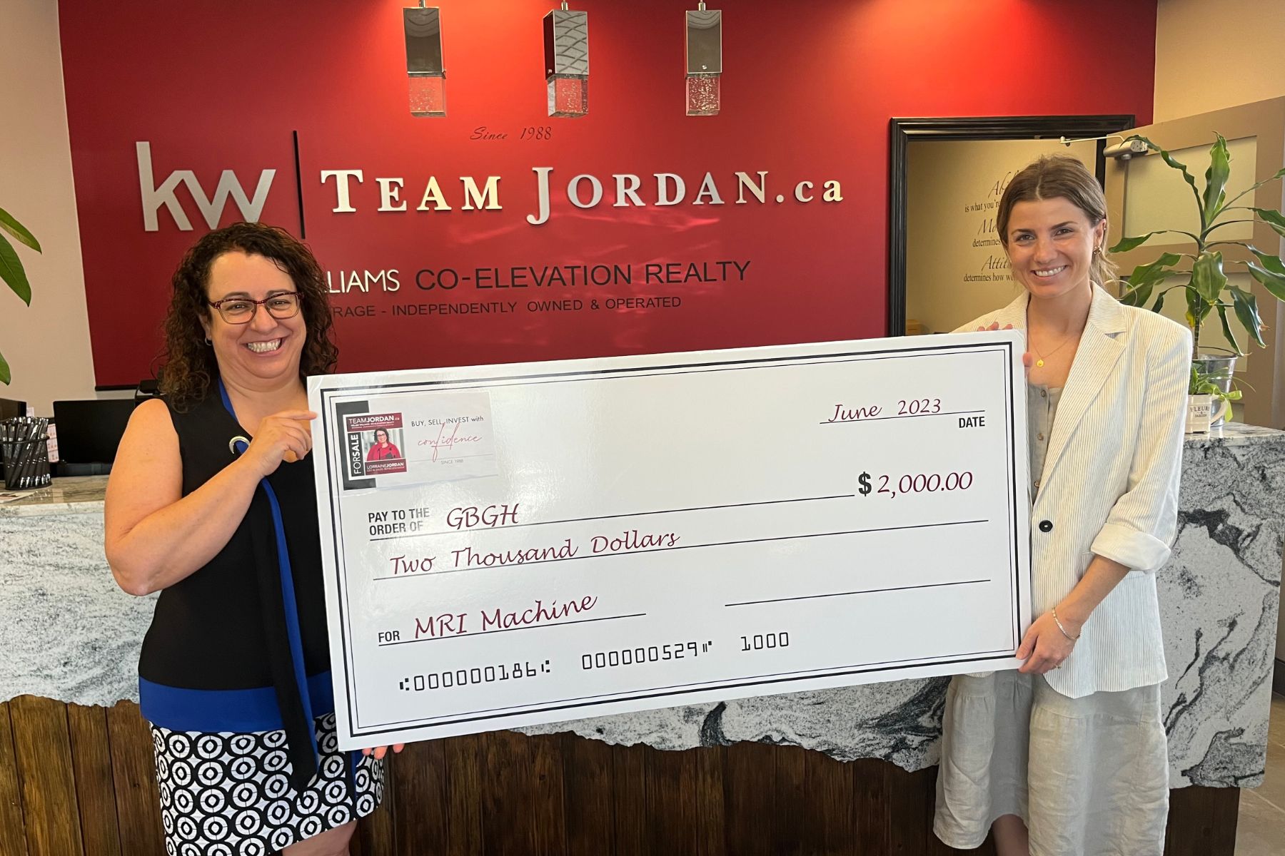 A women from Team Jordan holds up a giant cheque for $2,000 to donate to the GBGH MRI Fund. It is accepted by a women representing the GBGH Foundation.