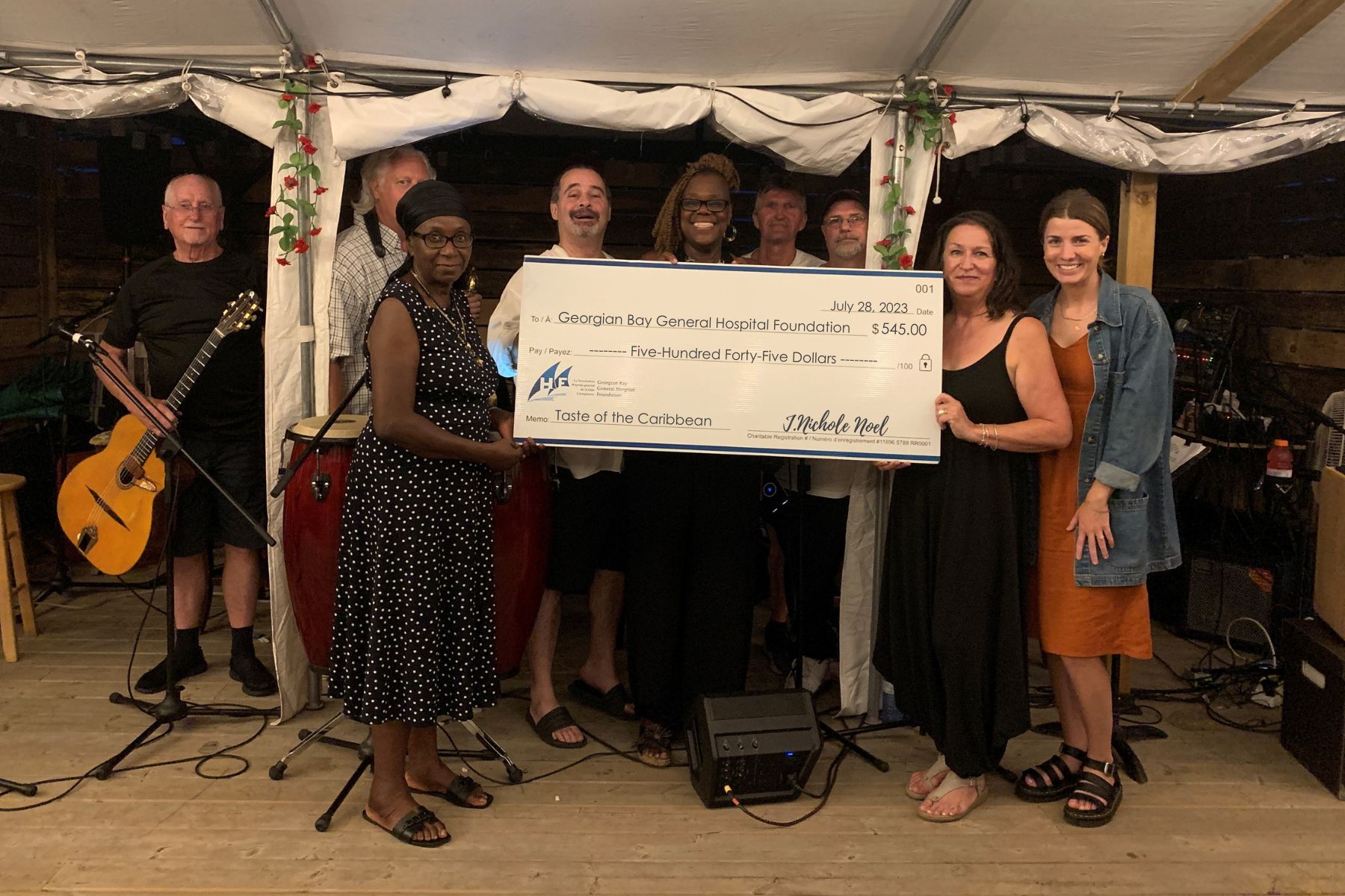 Four women and five men pose with a giant cheque made out to GBGH Foundation for $545 from the Taste of the Caribbean Event