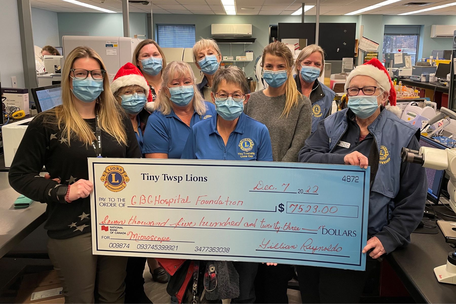 Nine people - many with Lions Club logos on their clothing hold a giant cheque for $7,523 for a microscope for the GBGH from the Tiny Township Lions club.