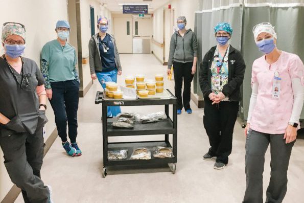 Six masked hospital workers standing near a cart with individual bowls of soup with lids