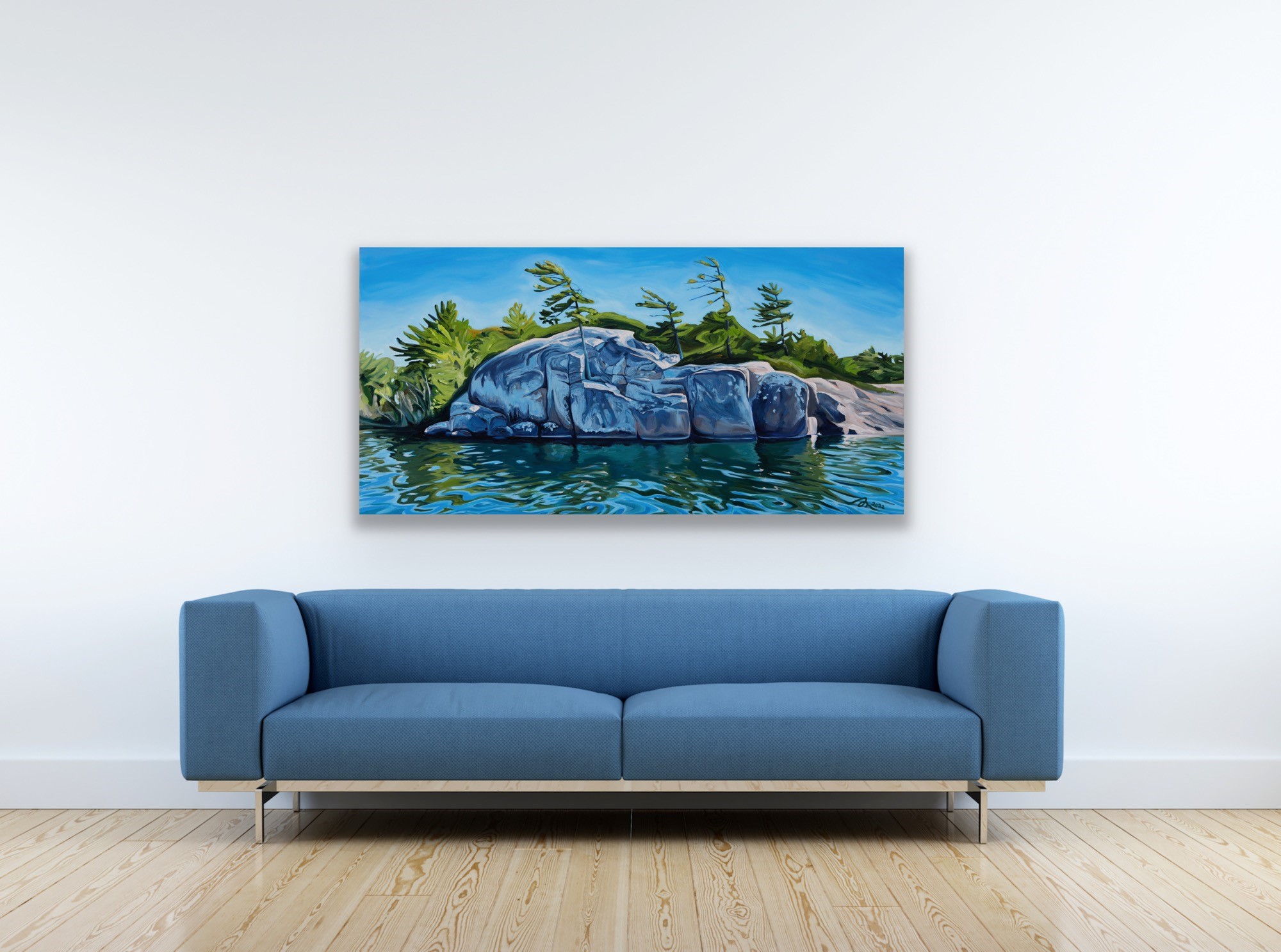 A blue couch on a light wood floor. Above hangs an original painting over Georgian Bay water, trees and rocks.