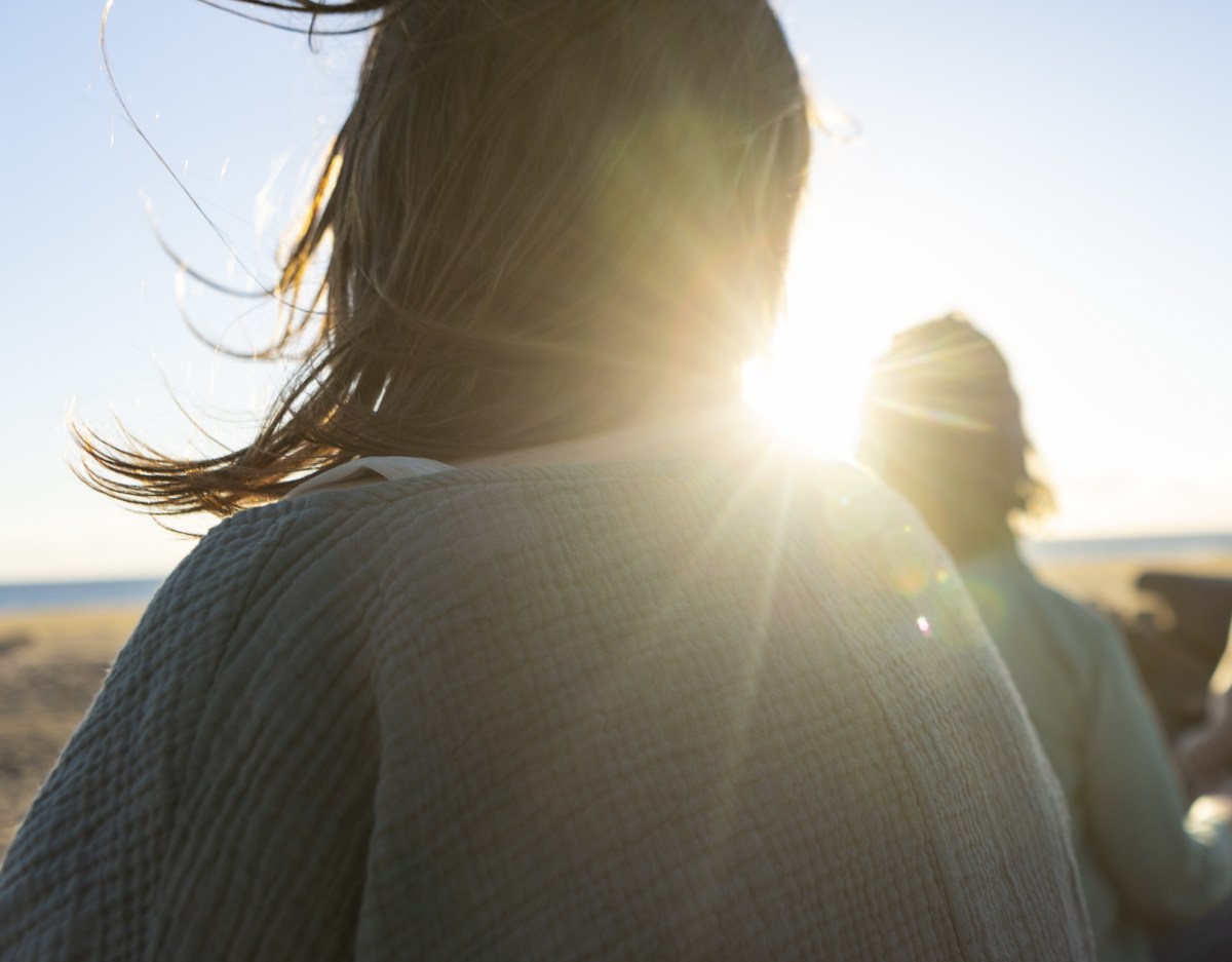 a woman outside facing the setting sun, with the sun visible next to her neck causing lens flare