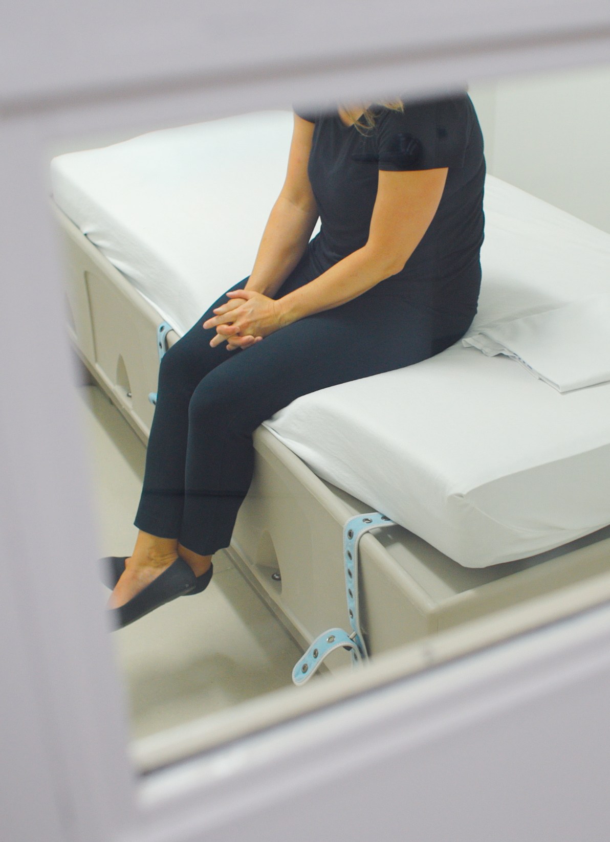 looking through a small door window to see someone sitting on hospital bed