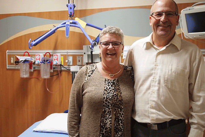 A man and a woman standing in front of a hospital bed with a rack hanging over the bed.
